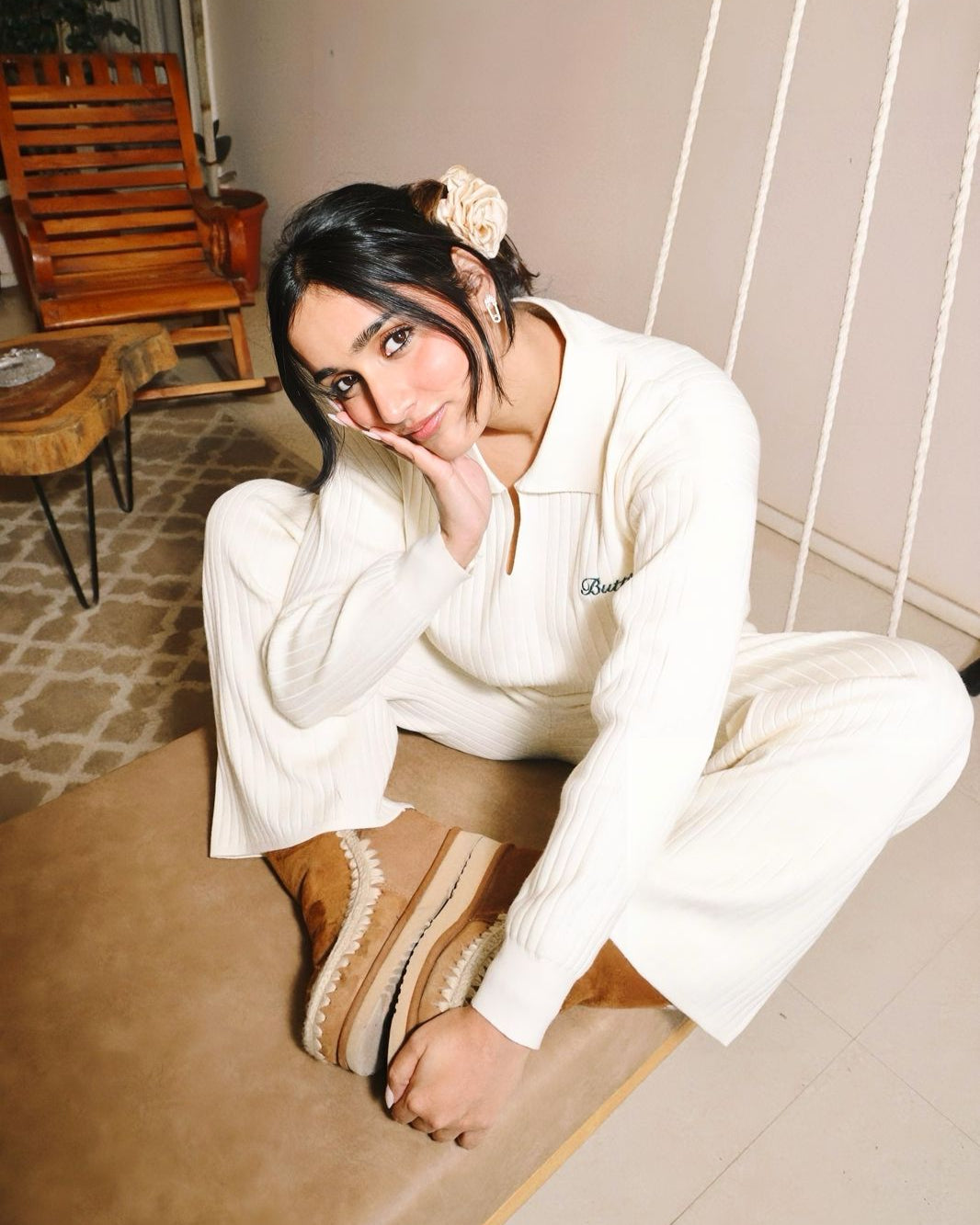 Woman in a white outfit sitting on a wooden floor with a neutral background