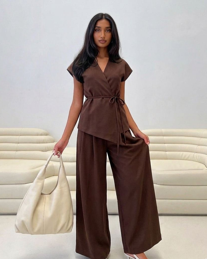 Woman in a brown outfit holding a cream bag against a white background