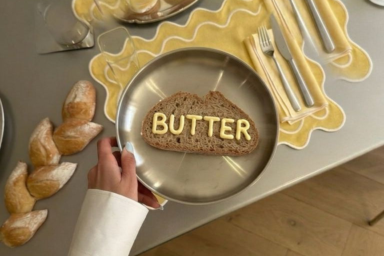 Person holding a plate with 'BUTTER' on a decorative table setting.